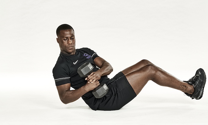 Man in black shorts and black training top performing dumbbell Russian twist