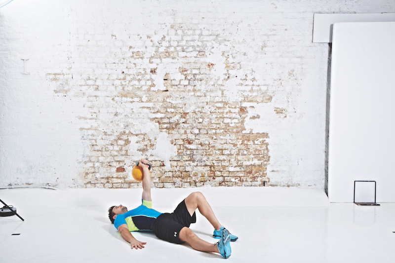 Man in blue top and black shorts performing kettlebell Turkish get-up