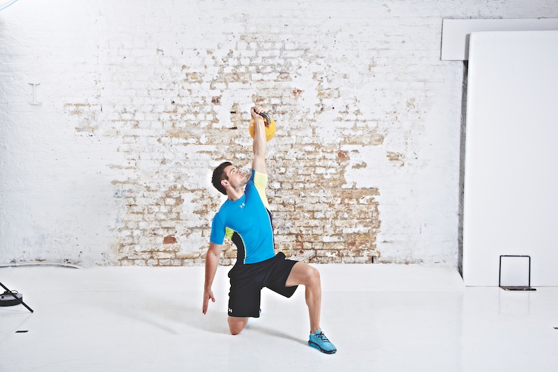 Man in blue top and black shorts performing kettlebell Turkish get-up