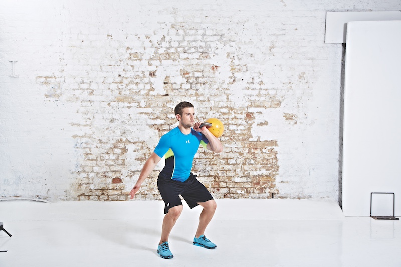 Man in blue top and black shorts performing kettlebell clean and press