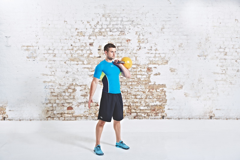 Man in blue top and black shorts performing kettlebell clean and press