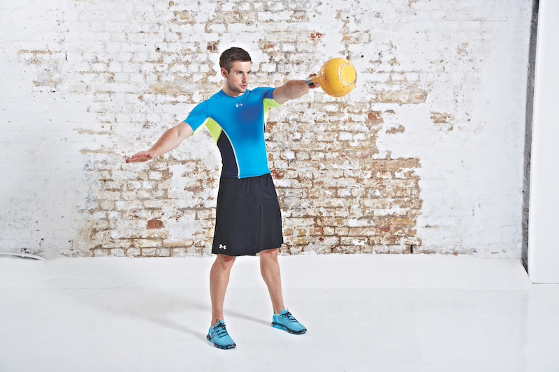 Man in blue top and black shorts performing kettlebell single-arm swing