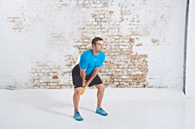 Man in blue top and black shorts performing kettlebell swing