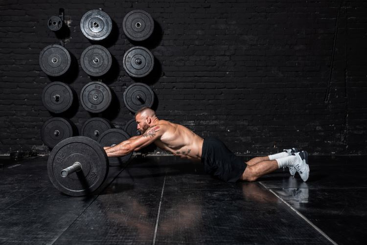 Man in a gym performing a barbell abs rollout