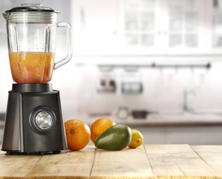 Blender on wooden surface with pieces of fruit next to it