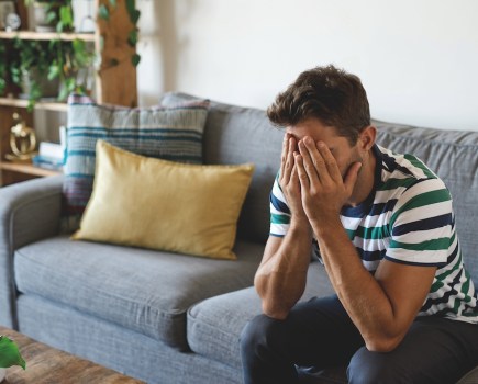 Young man sat on sofa with head in hands