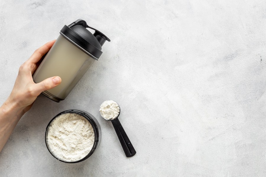 Sport shaker bottle in hands and whey protein in jar. Fitness and gym diet nutrition