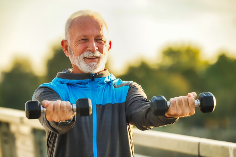 Elderly man exercising outside with pair of dumbbells