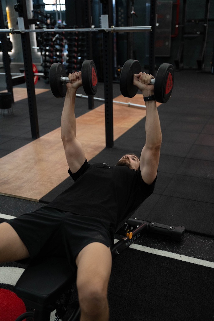 PT demonstrating how to perform a dumbbell bench press