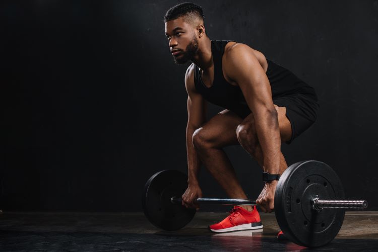 A man squatting to lift a barbell wearing red lifting shoes