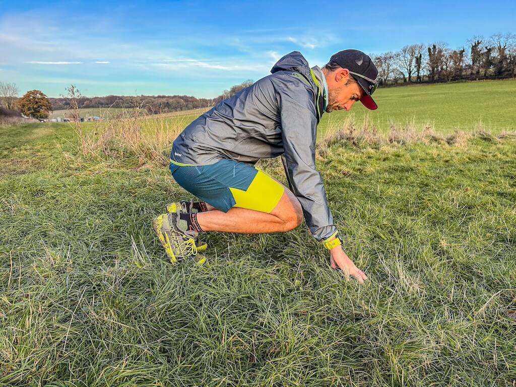 Running coach Simon James performing plantar fascia stretch in a field after a trail run