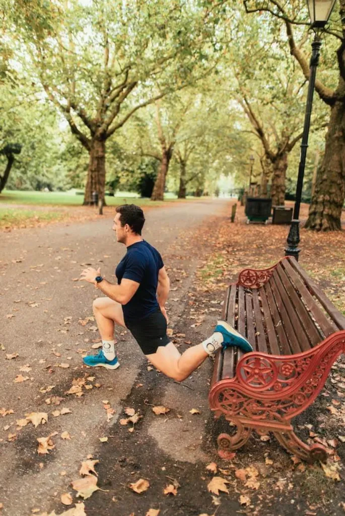 Man performing Bulgarian split squat on a park bench