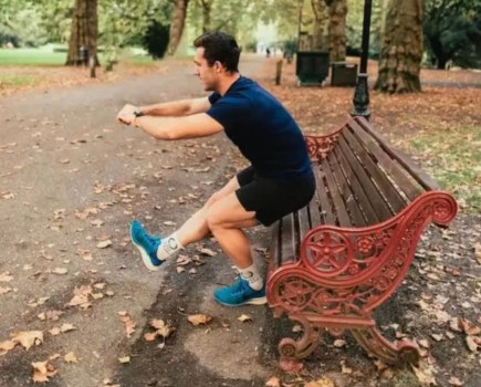 Man by a park bench performing a single leg squat
