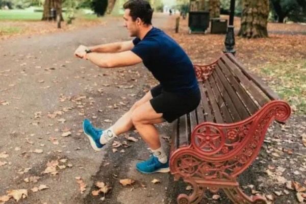 Man by a park bench performing a single leg squat