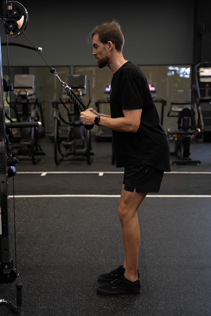 PT demonstrating how to perform a triceps rope pushdown in a workout routine for beginners