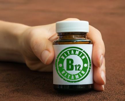 A hand holding a bottle of Vitamin B12 tablets