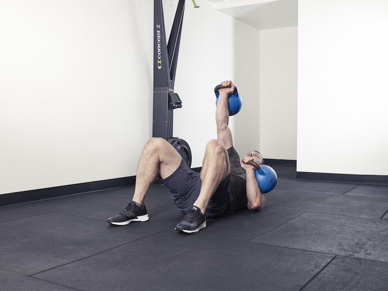 fitness model demonstrating how to perform a kettlebell rolling thunder abs exercise