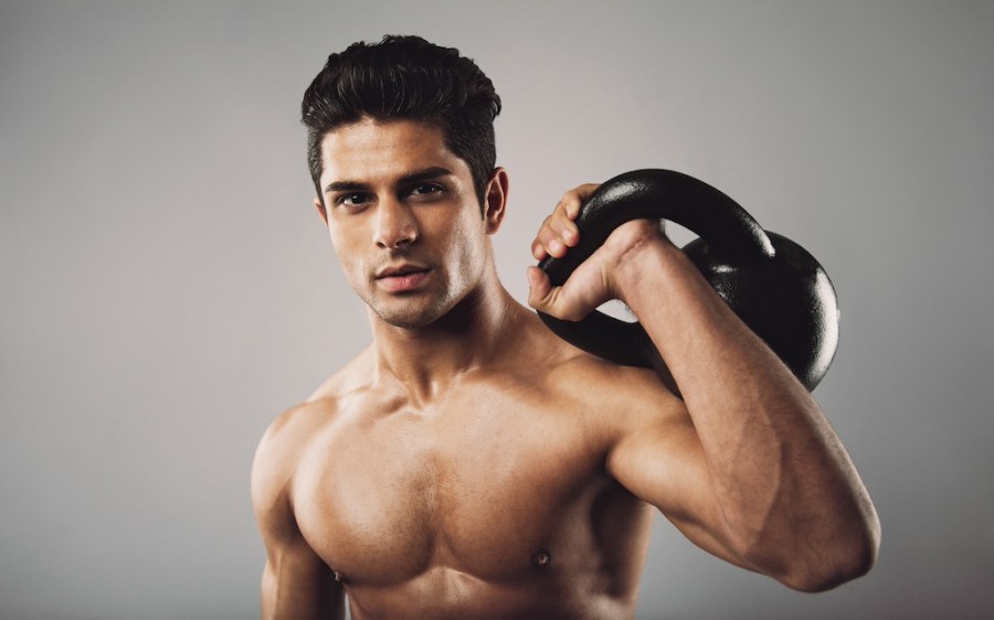 topless man holding kettlebell on one shoulder