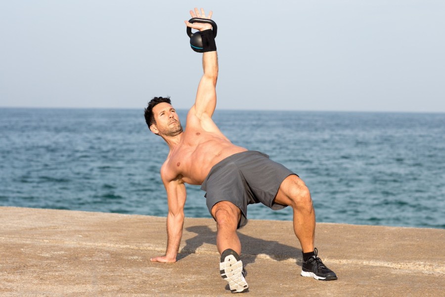 topless man exercising with kettlebell on the beach