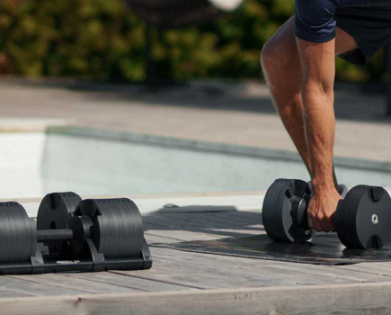 Close-up of a man leaning down to pick up adjustable dumbbells