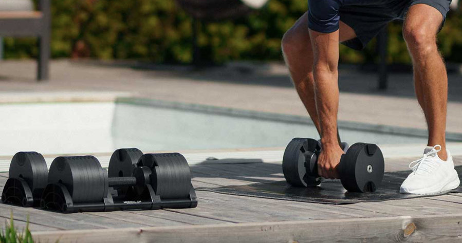 Close-up of a man leaning down to pick up adjustable dumbbells