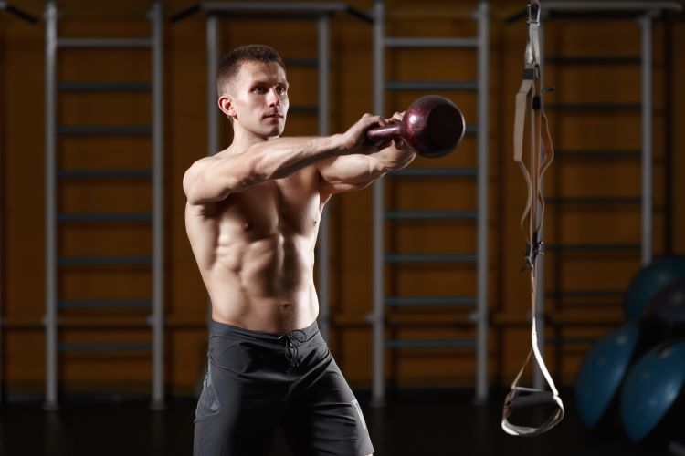 Shirtless man swinging a kettlebell