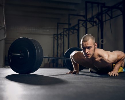 Man performing push-ups next to a barbell