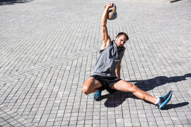 Man performing a Turkish get-up outdoors with a kettlebell