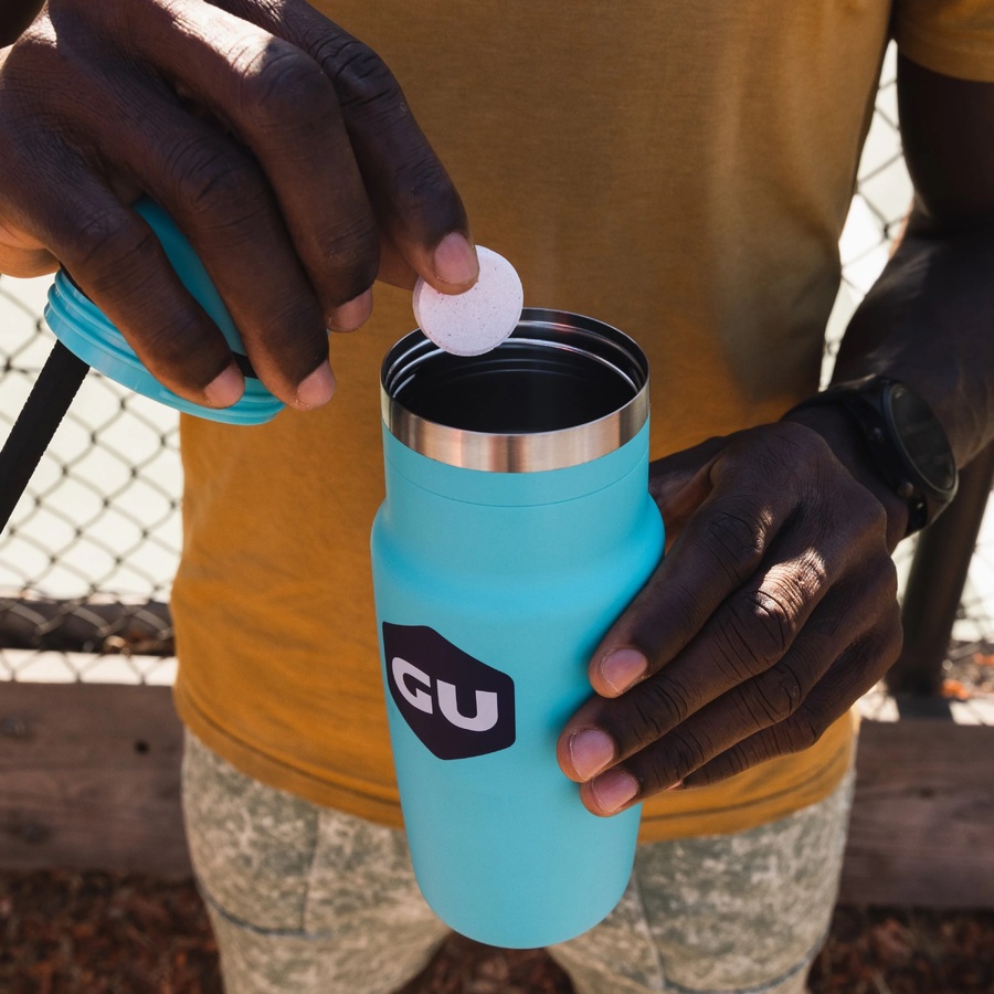 man dropping gu electrolyte tablet into blue water bottle after workout