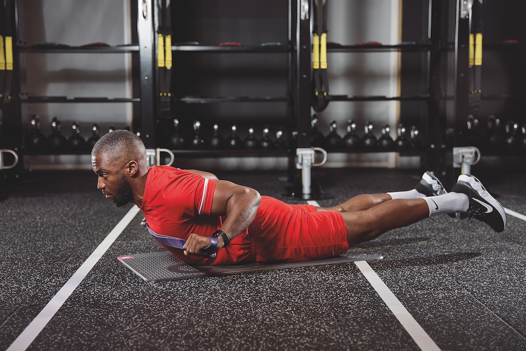 man in red top and red shorts doing a superman with banded row in the gym as part of a full-body circuit