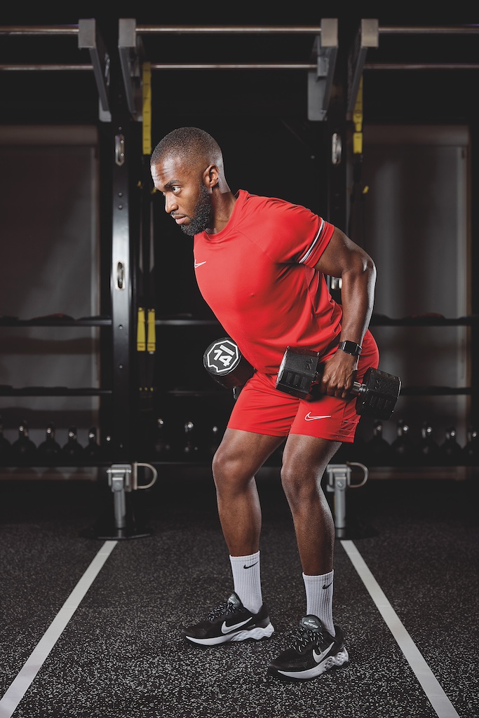 man in red top and red shorts doing a dumbbell hinged row in the gym as part of a full-body circuit