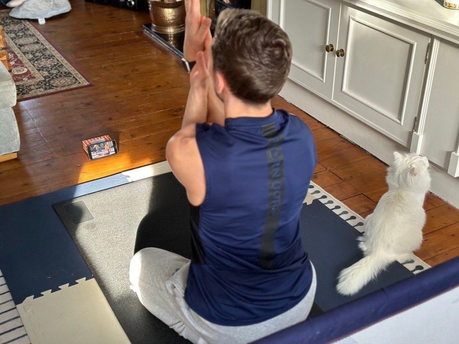 man in sports clothes performing mobility pose on living room floor