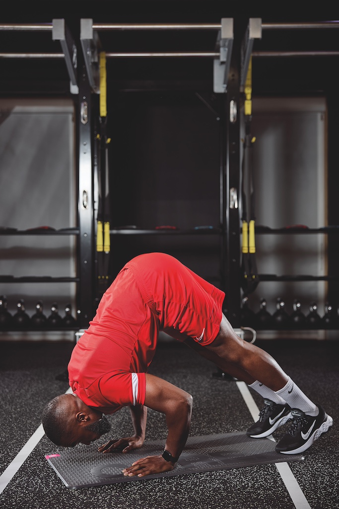 man in red top and red shorts doing a pike push-up in the gym