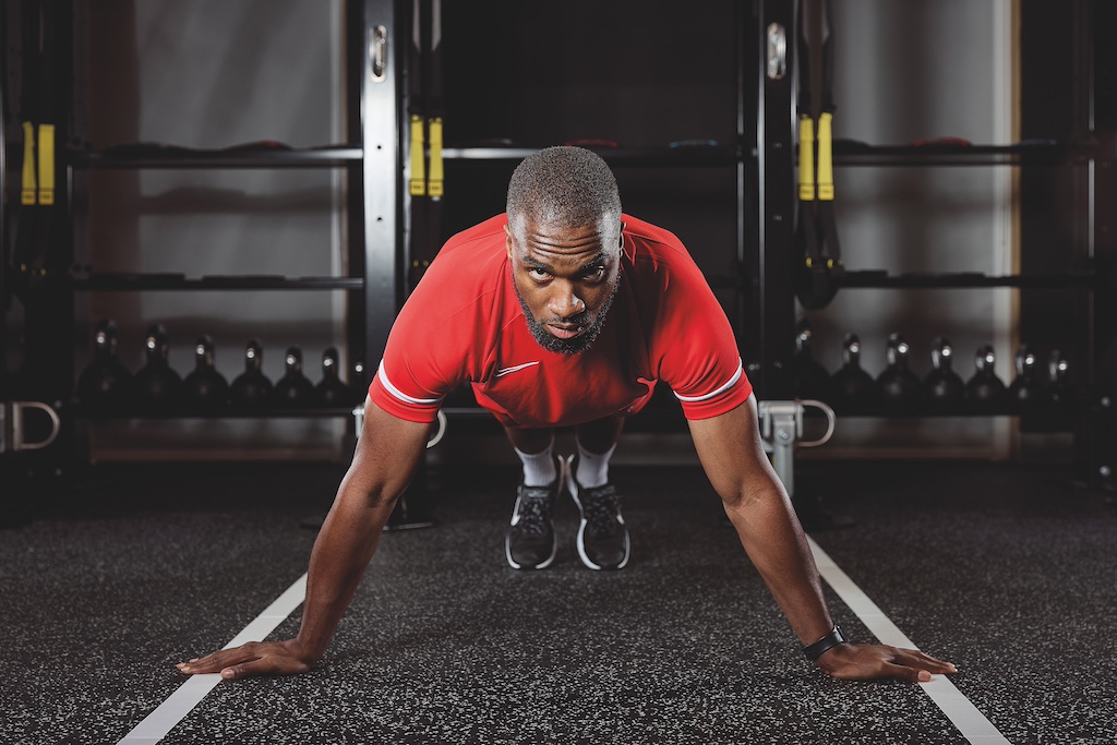 man in red top and red shorts doing a typewriter push-up in the gym as part of a full-body circuit