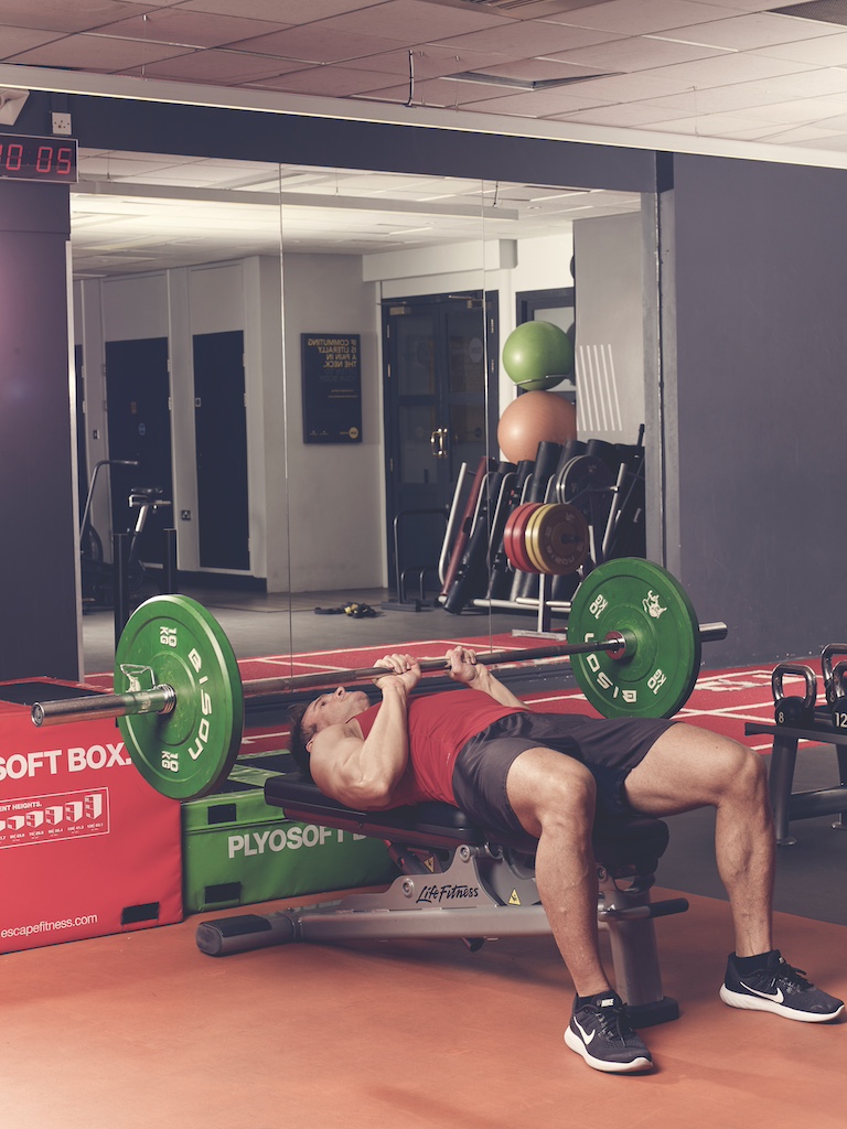 man in red vest and black shorts performing close-grip bench press in the gym