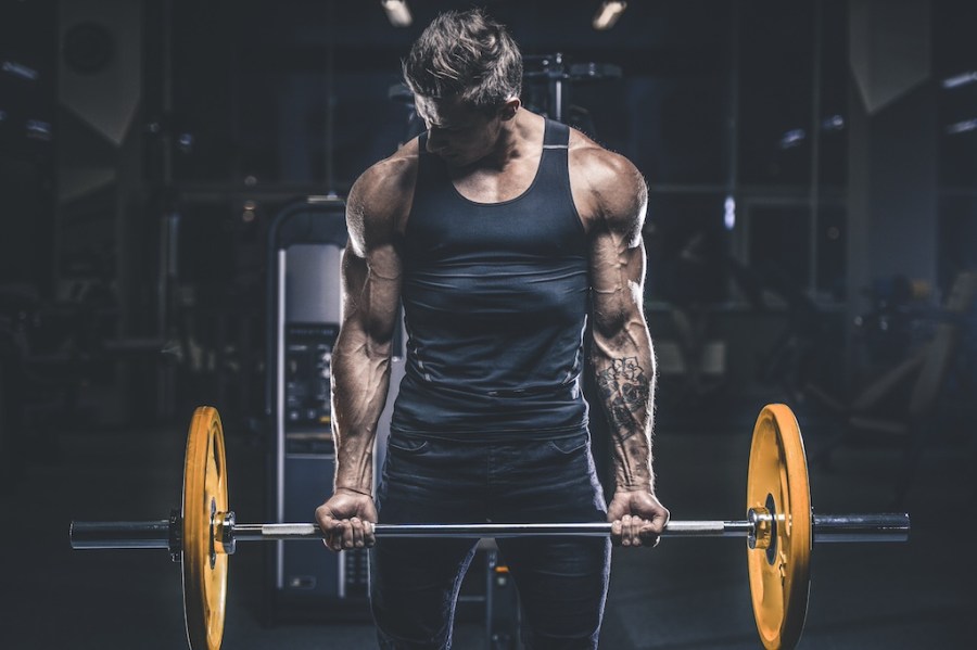 man in vest performing bicep curl with barbell