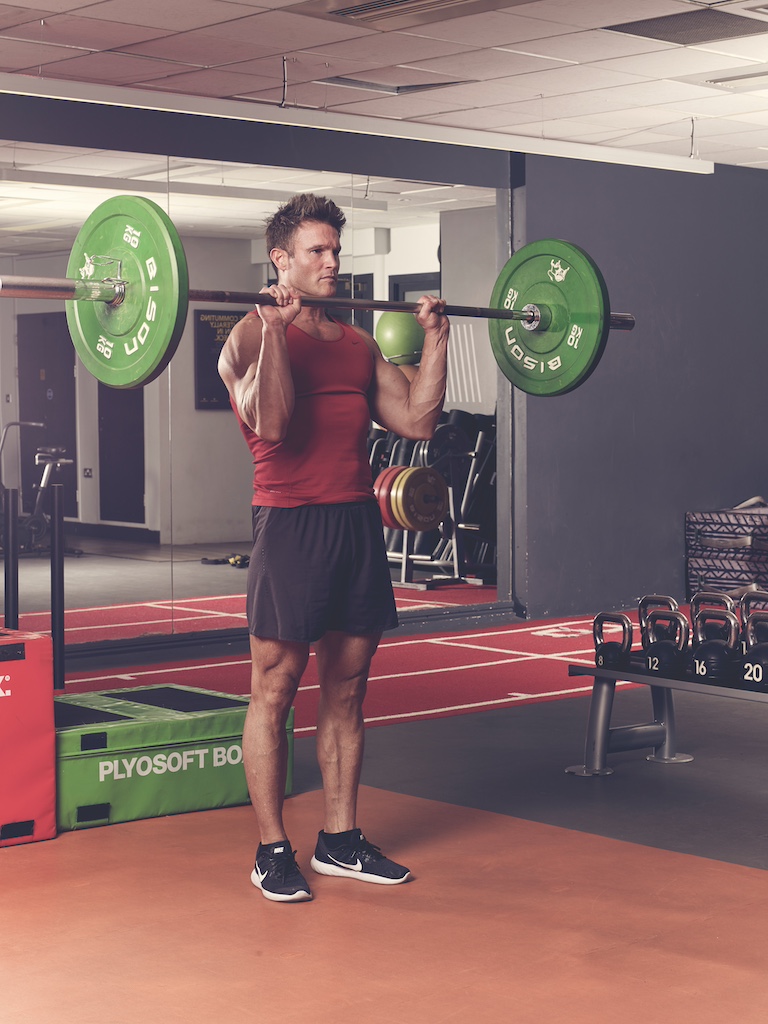 man in red vest and black shorts performing barbell reverse curl in the gym