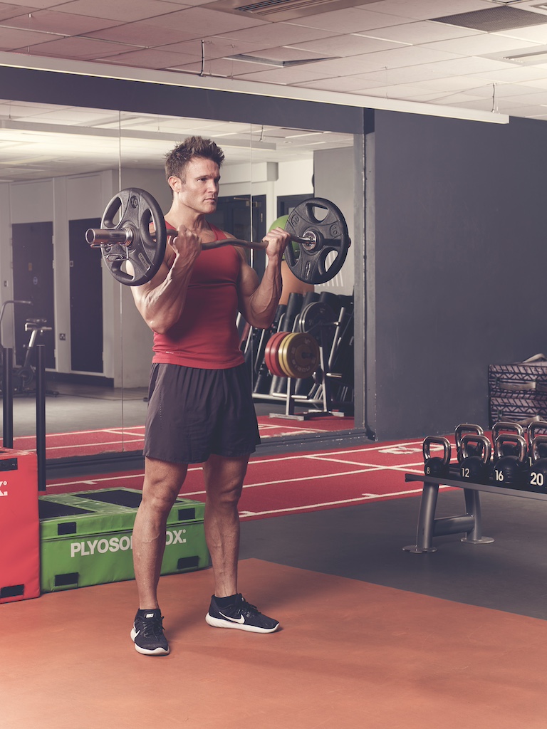 man in red vest and black shorts performing EZ-bar curl in the gym – one of the best barbell arms exercises