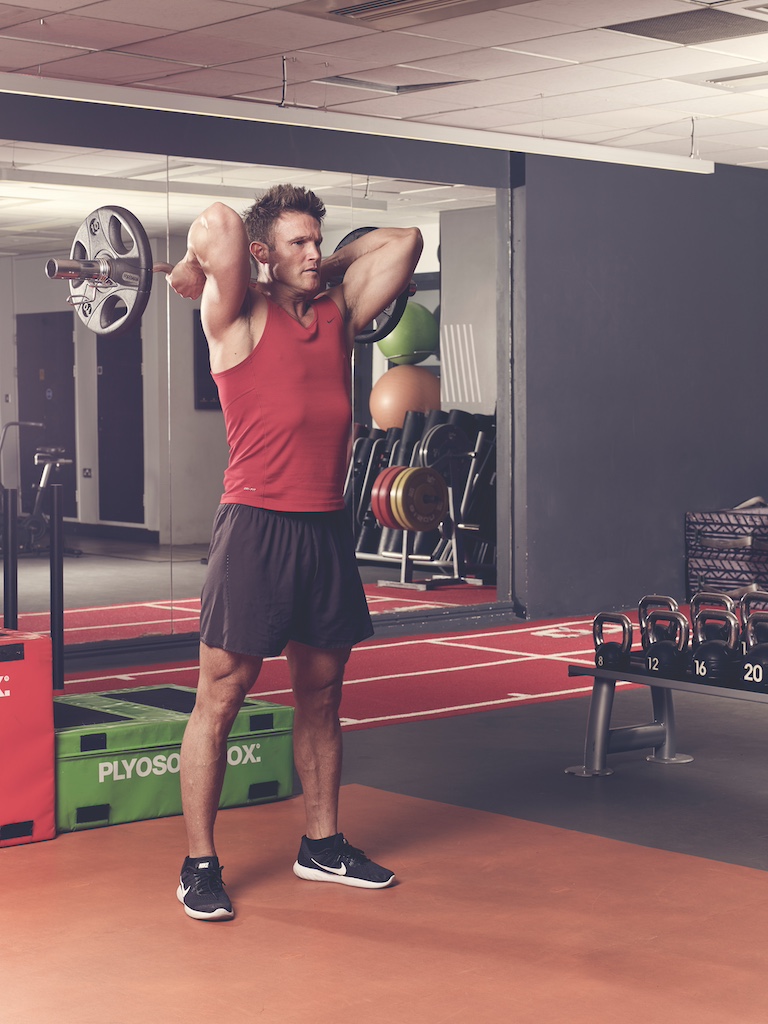 man in red vest and black shorts performing overhead triceps extension in the gym