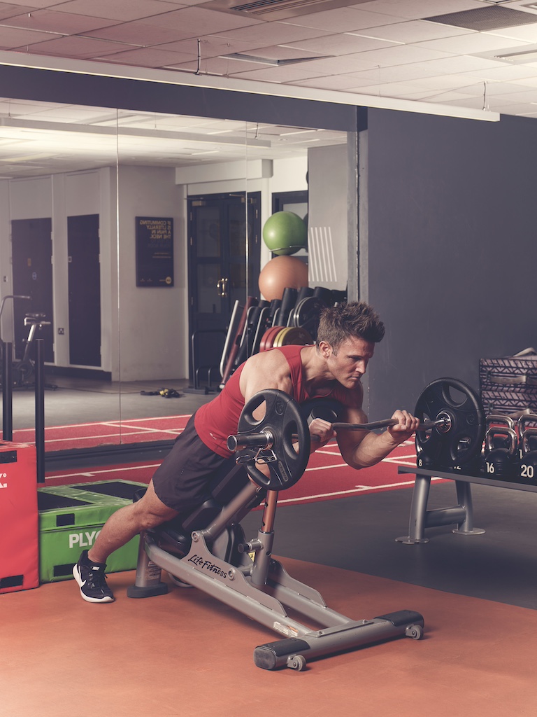 man in red vest and black shorts performing EZ-bar prone incline reverse curl in the gym