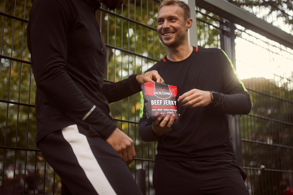 Two fit friends eating Jack Link's beef jerky outside