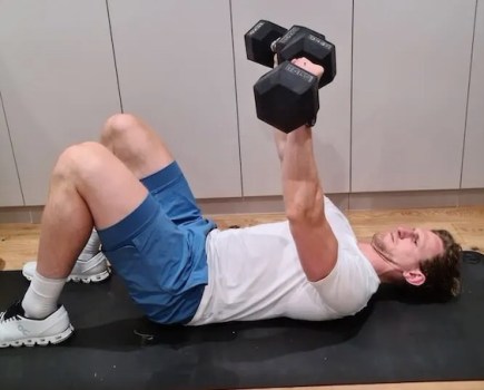 Man performing dumbbell presses on an exercise mat