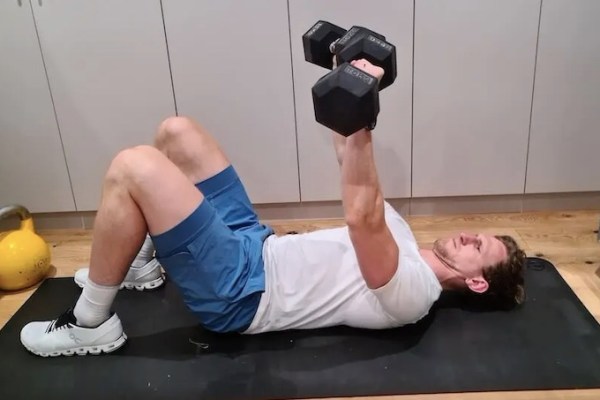 Man performing dumbbell presses on an exercise mat