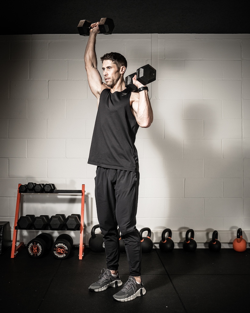 Personal trainer demonstrating how to do a dumbbell alternating shoulder press