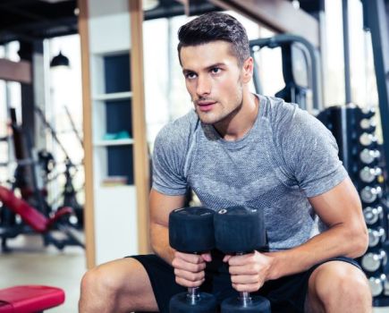 Man sitting in a gym holding dumbbells