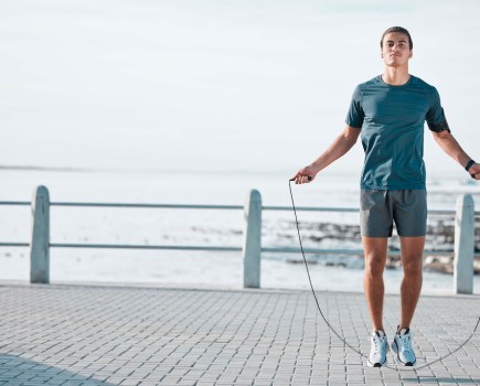 Skipping rope, mockup and man training by the beach for his outdoor morning exercise, workout and fitness routine. Athlete, cardio and male jump by the ocean or sea for wellness lifestyle