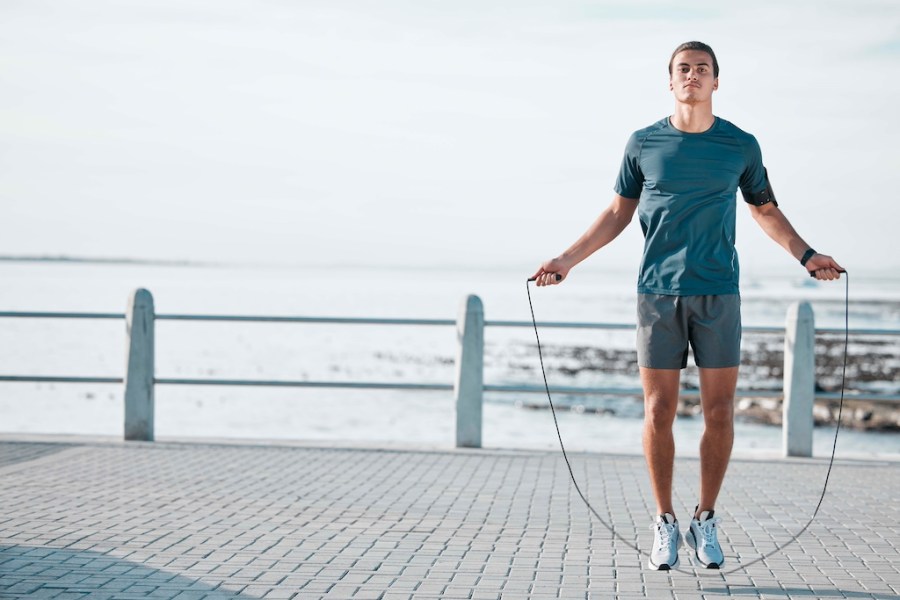 Skipping rope, mockup and man training by the beach for his outdoor morning exercise, workout and fitness routine. Athlete, cardio and male jump by the ocean or sea for wellness lifestyle