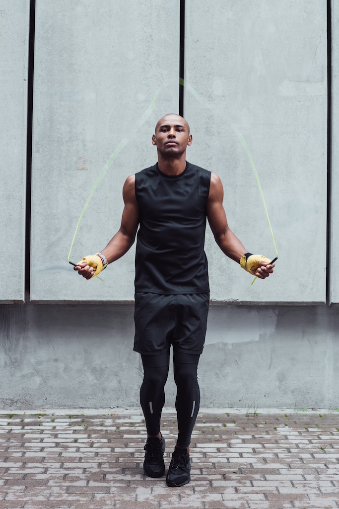 Full length of young man in sportswear exercising against grey background outdoors