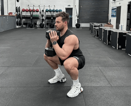 Man performing a dumbbell goblet squat in a gym