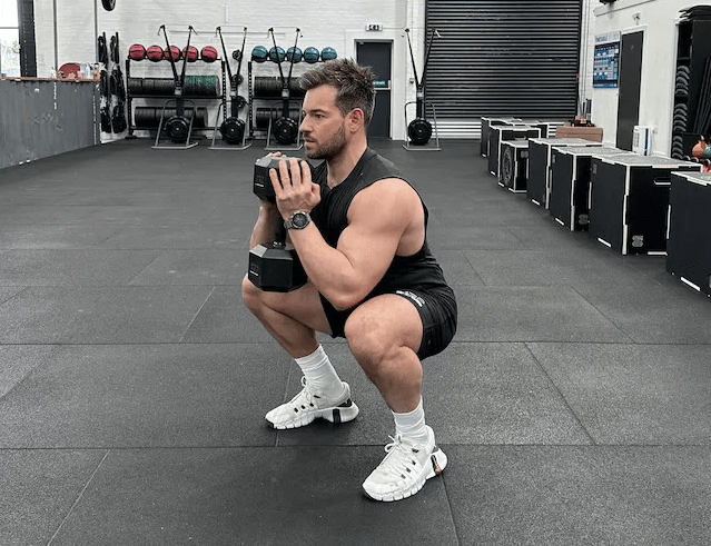 Man performing a dumbbell goblet squat in a gym